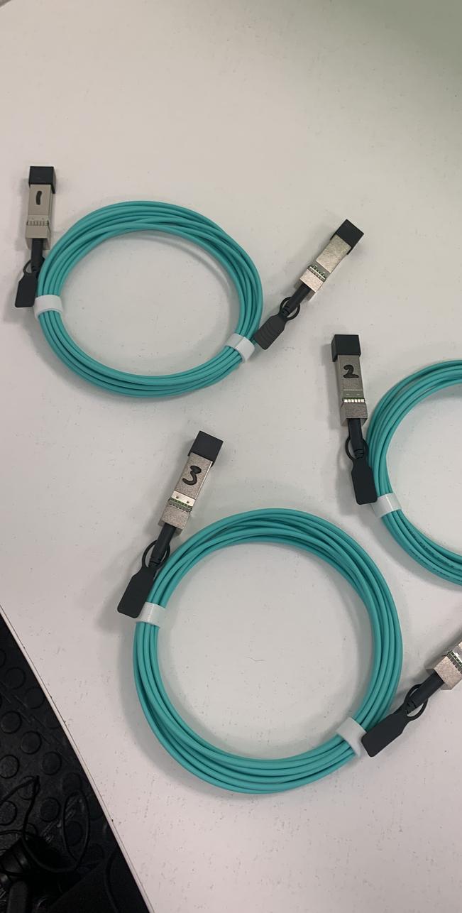 Three aqua active optical cables in loops on a white desk