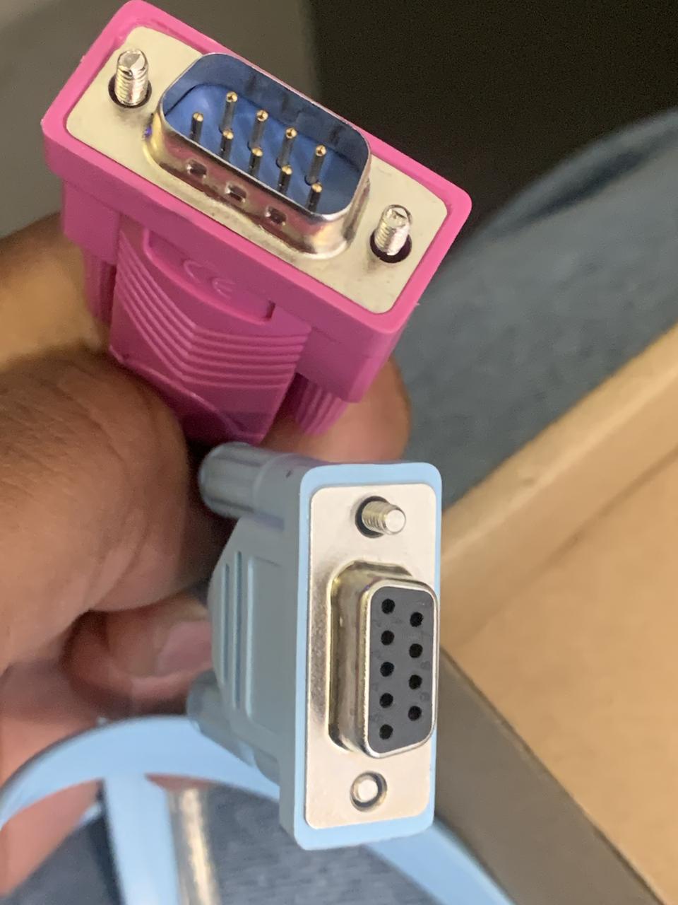 Hand holding a pink serial console adapter and a light-blue console cable
