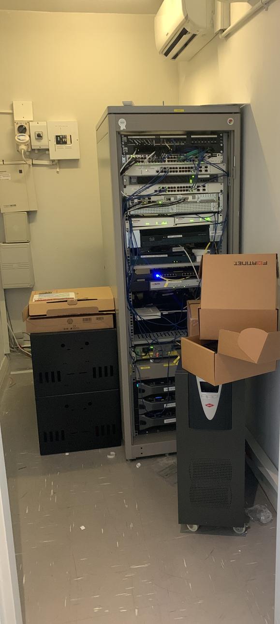 Small office comms room with a network rack, UPS and boxes