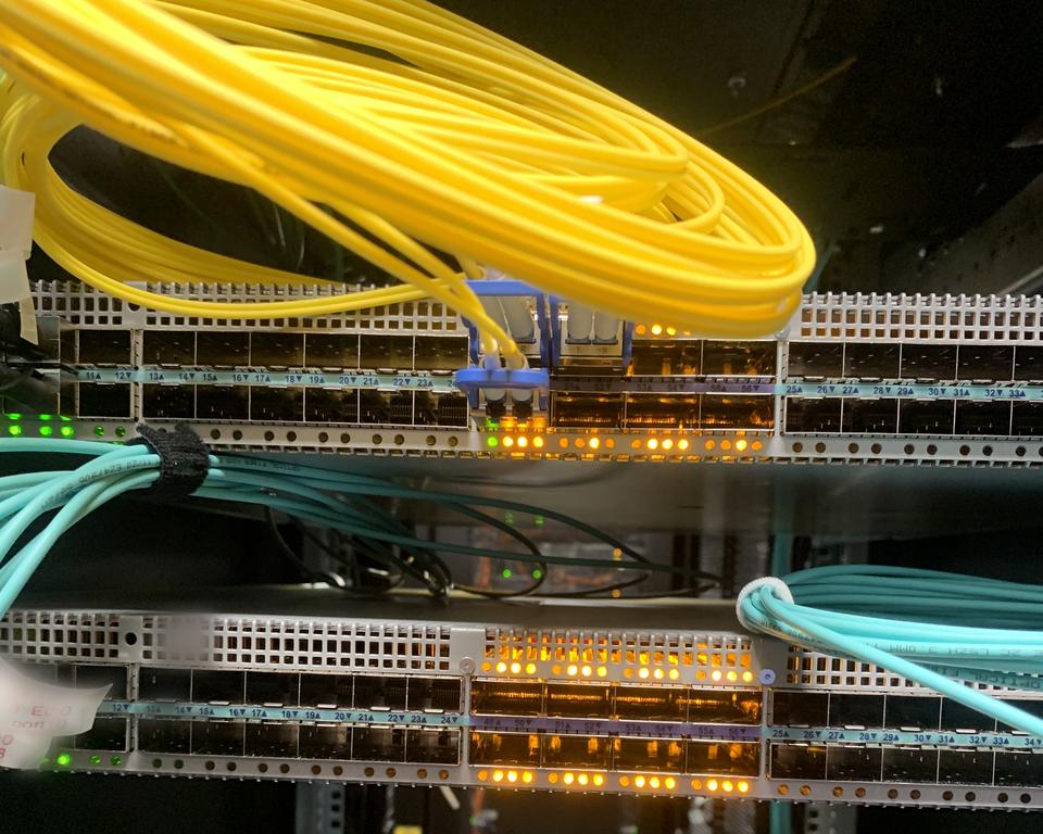 Yellow single-mode fibre and aqua patch leads on data centre switches with amber port lights