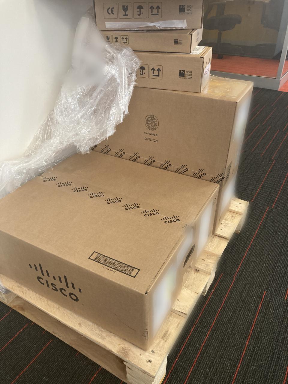 Boxed Cisco networking equipment on a pallet, shipping labels blurred